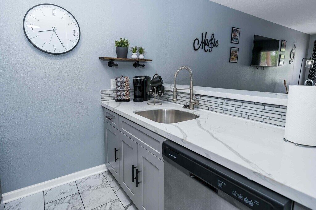 A modern kitchen with a sink, dishwasher, and a clock on the wall.