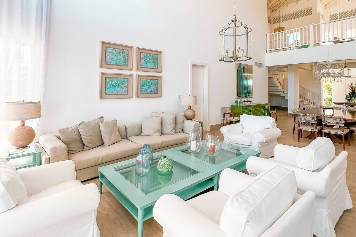 A spacious living area with a high ceiling, a sofa set, a coffee table, and artwork on the wall.