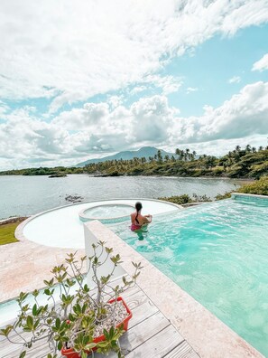 A pool with a person in a pink swimsuit, surrounded by tropical vegetation and a mountain in the background. - Peninsula Esmeralda Luxury Hotel & Villas (Puerto Plata)