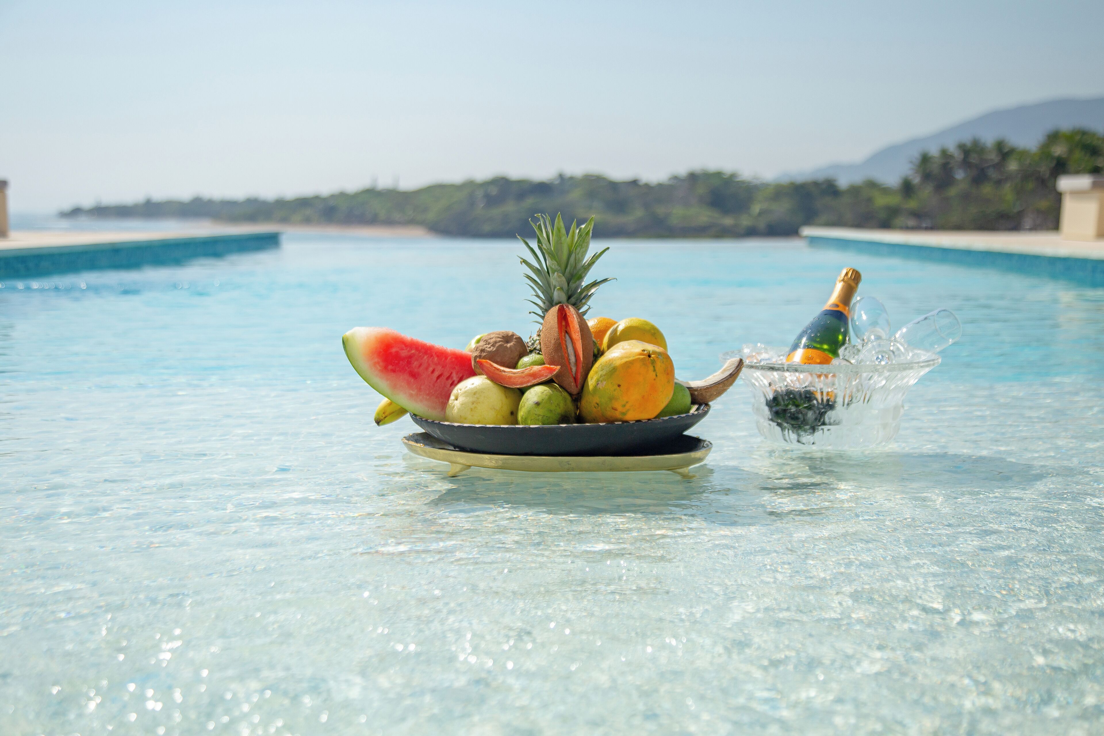 Un panier de fruits et une bouteille de champagne au bord d’une piscine.