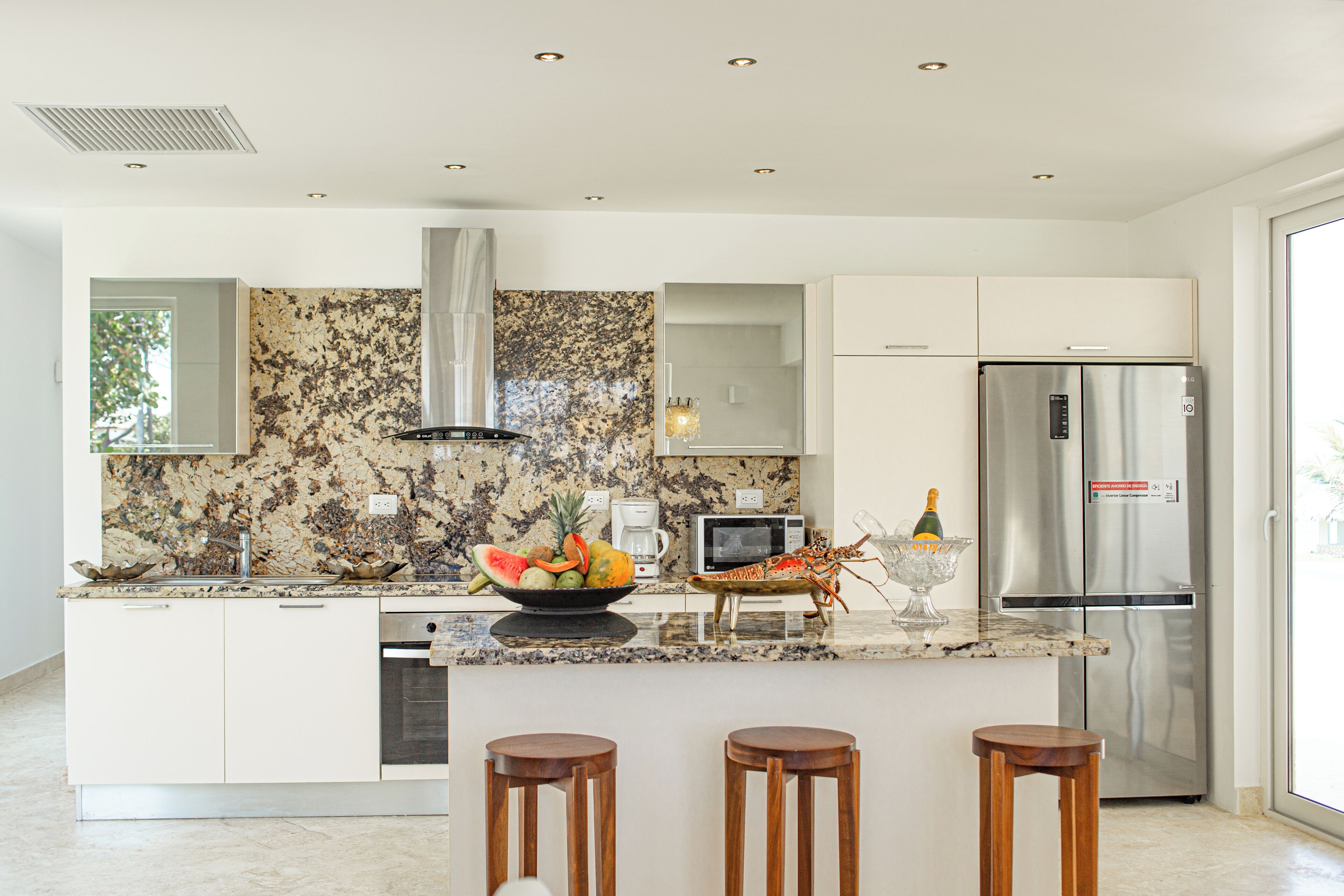 A modern kitchen with a granite countertop, stainless steel appliances, and a central island with stools.