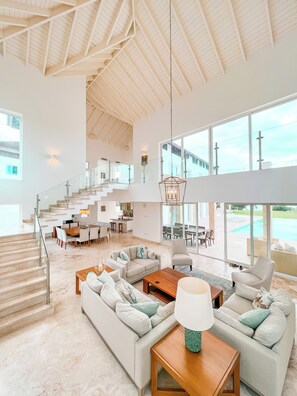 A spacious living area with a high ceiling, a staircase leading to upper floors, and large windows offering views of the outdoors. - Peninsula Esmeralda Luxury Hotel & Villas (Puerto Plata)