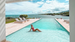A pool area with a person relaxing in the water, lounge chairs, and a view of the ocean. - Peninsula Esmeralda Luxury Hotel & Villas (Puerto Plata)