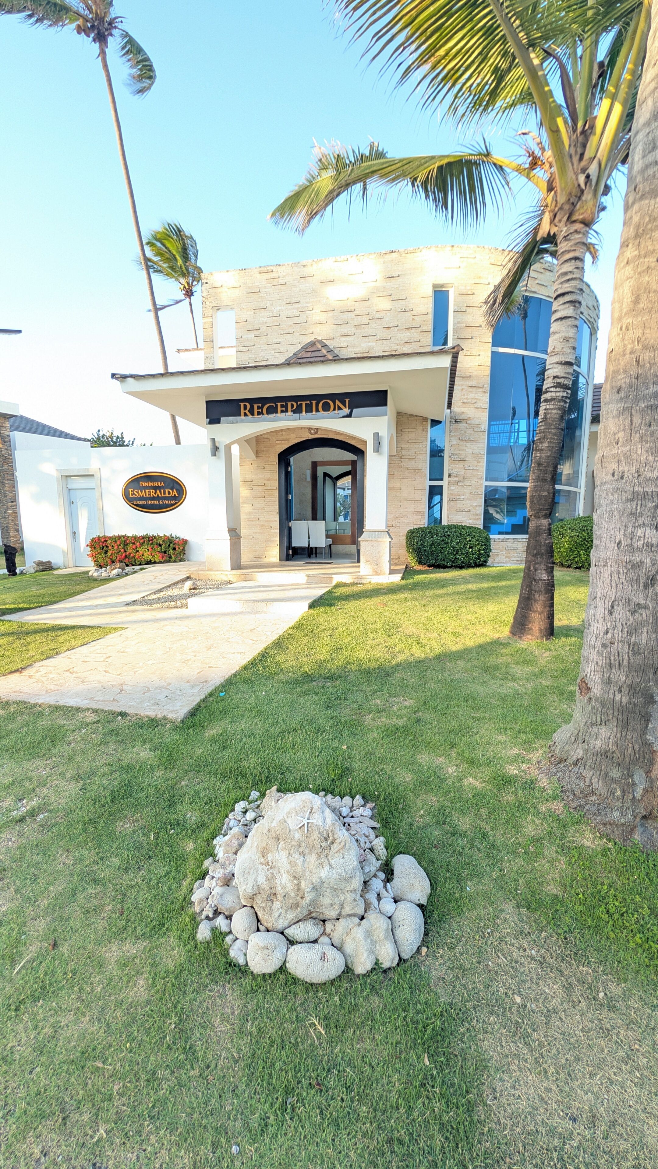 A building with a reception area, palm trees, and a stone pathway leading to the entrance.