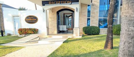 A building with a reception area, palm trees, and a stone pathway leading to the entrance.