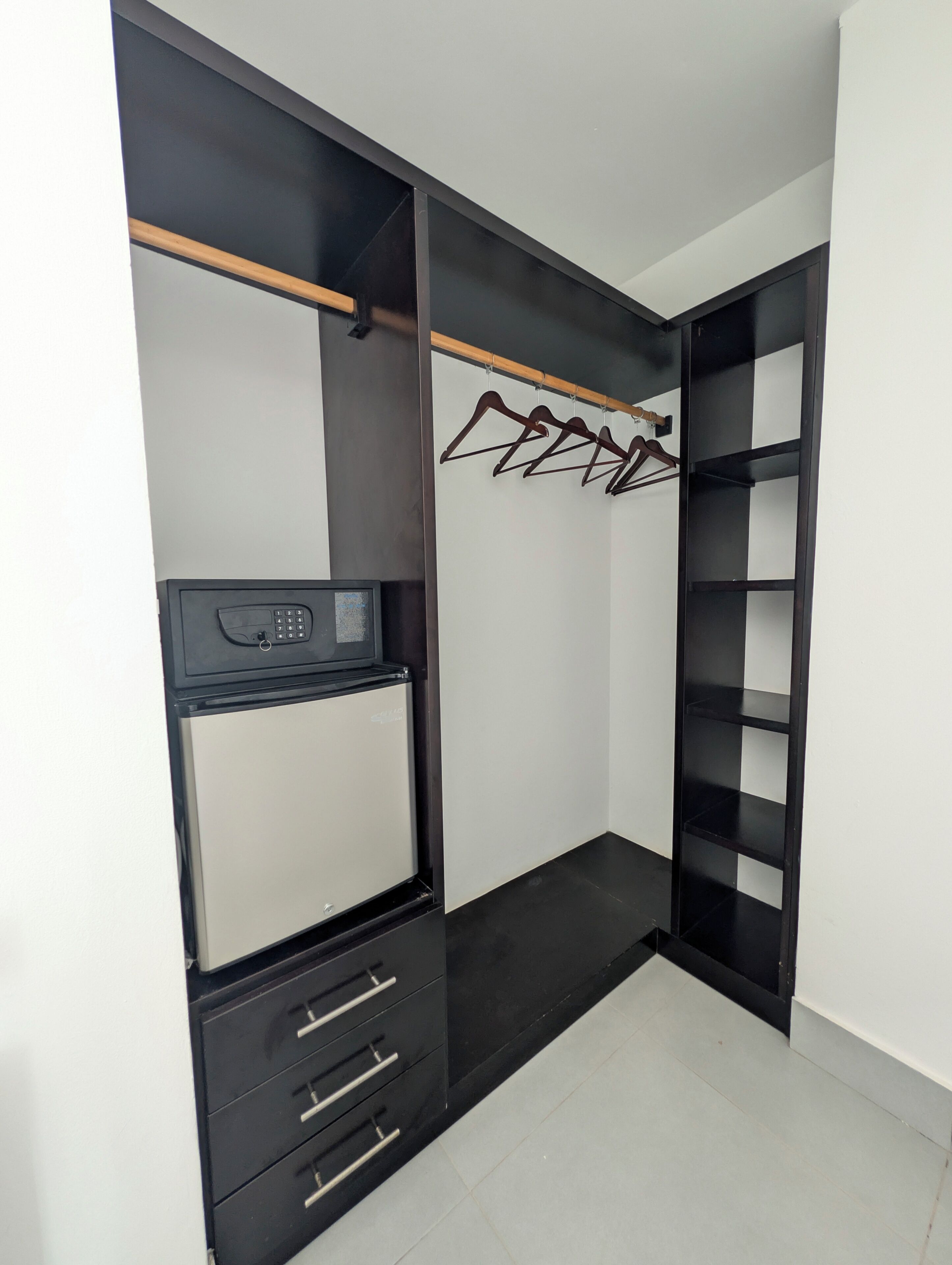 A walk-in closet with a black and white color scheme, featuring a hanging rod, shelves, and drawers.
