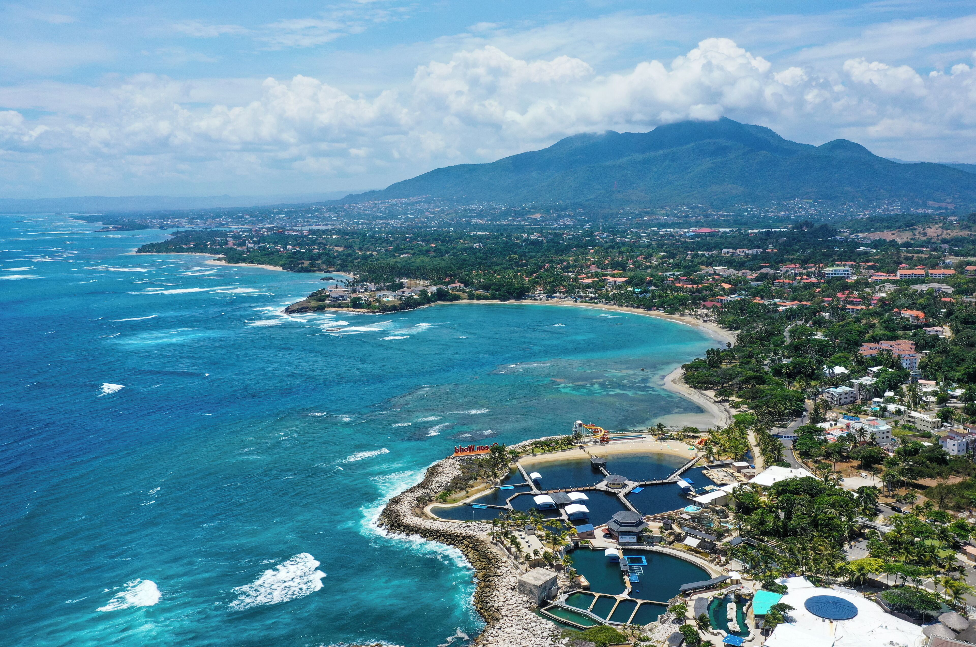 An aerial view of a coastal resort with a marina, beach, and mountainous backdrop.