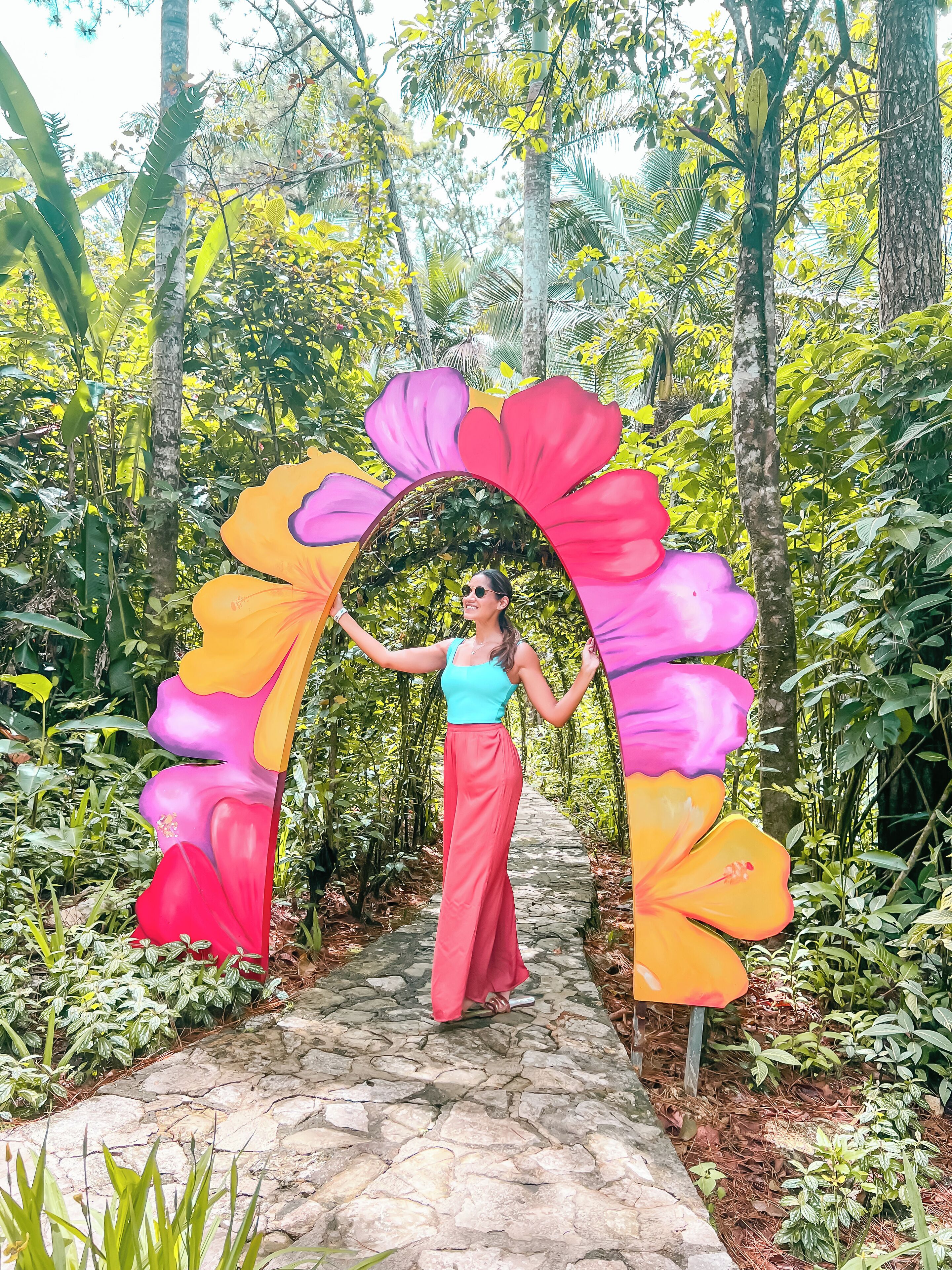 A person standing under a colorful floral archway in a lush garden setting.