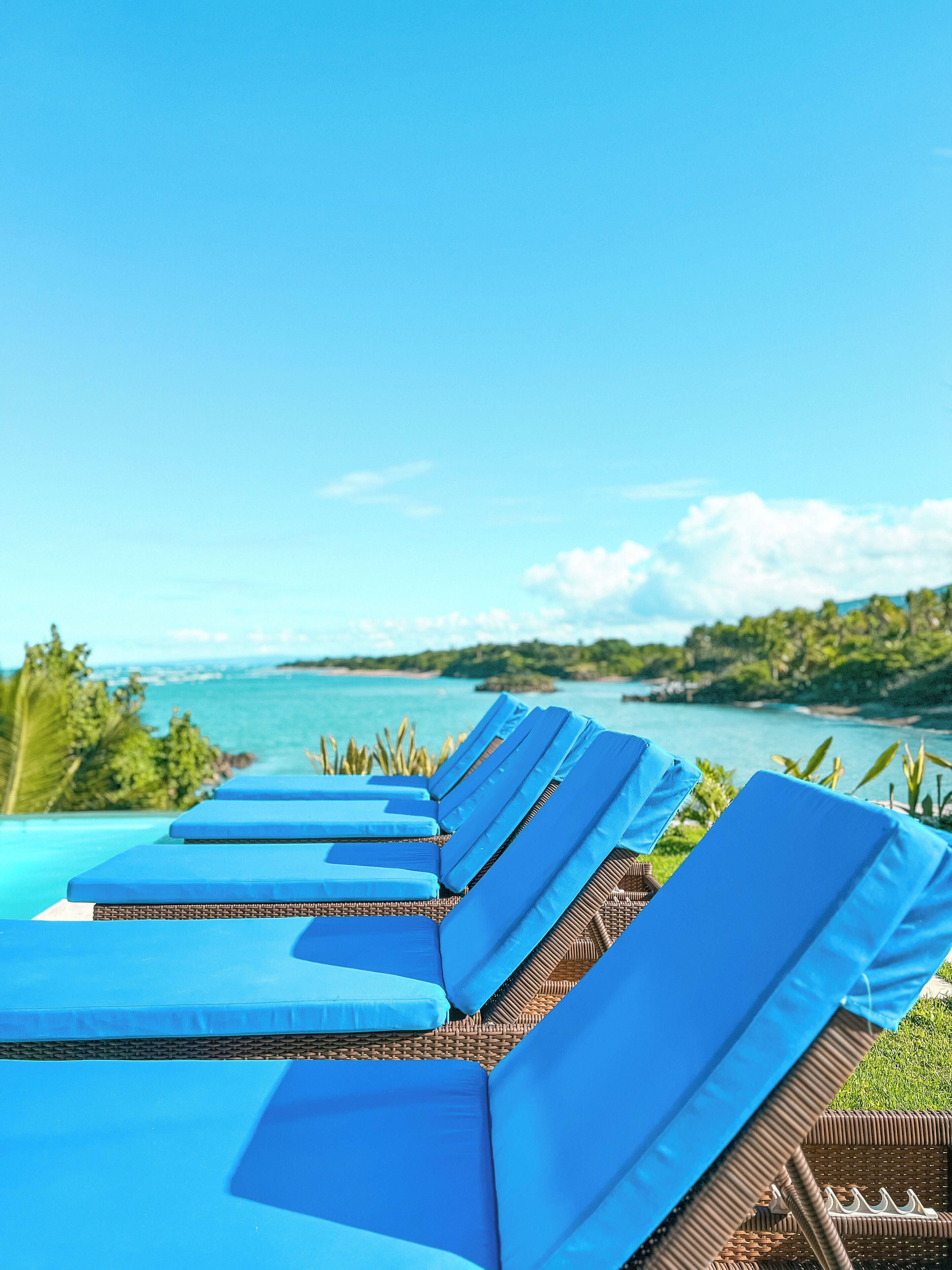 A row of blue lounge chairs with a view of a clear blue sky and a calm sea.