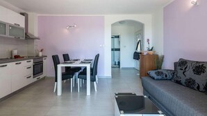 Een moderne woonkamer met een grijze bank, een eettafel met stoelen, een keuken met kasten en een fornuis, en een badkamer zichtbaar door een boog.