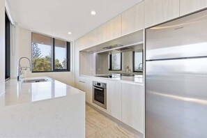 Une cuisine moderne dotée d’un grand îlot central, d’appareils électroménagers en acier inoxydable et offrant une vue sur l’extérieur.