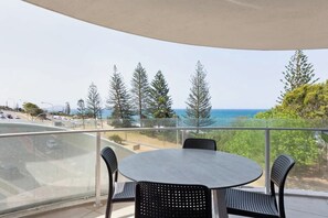 Ein Balkon mit rundem Tisch und Stühlen mit Blick auf eine Küstenstraße und den Ozean.