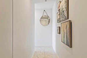 Un couloir avec un grand miroir suspendu, des œuvres d’art encadrées et un sol carrelé.