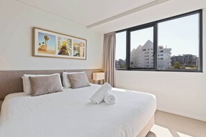 Ein Hotelzimmer mit einem großen Bett, einem Fenster mit Blick auf die Stadt und einem gerahmten Bild an der Wand.