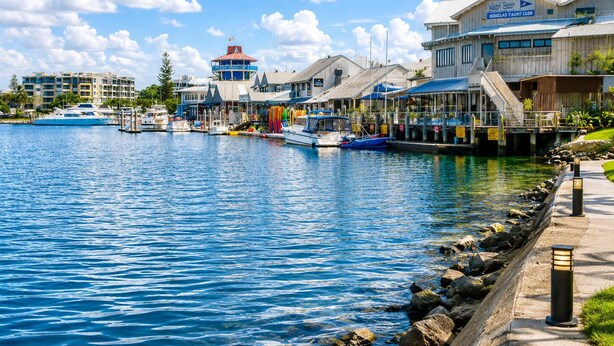 Una marina con barcos amarrados, un edificio que dice 'DOUGLAS YACHT CLUB' y un paseo marítimo.