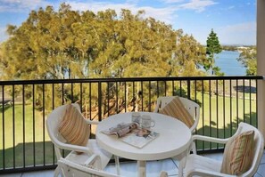 A balcony with a table and chairs, overlooking a golf course and a body of water. - Beachport 11 River Apt Mooloolaba (Mooloolaba)