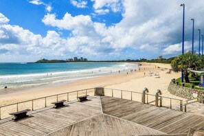 Une plage avec une promenade en bois, des bancs et une vue sur l’océan et les bâtiments situés au loin.