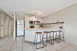 A modern kitchen with a central island, bar stools, a microwave, oven, and a refrigerator.