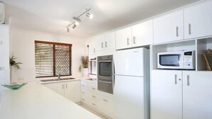 Una cocina moderna con armarios blancos, horno empotrado, microondas y ventana con persianas.