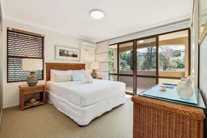 A bedroom with a bed, a nightstand, a lamp, a wicker basket, and a large window with a view. - Beachport 16 Waterfront Views Apt (Mooloolaba)