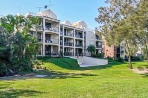 A multi-story hotel with balconies, a well-maintained lawn, and a clear sky. - Beachport 16 Waterfront Views Apt (Mooloolaba)