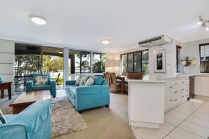 A modern living room with a sofa, a coffee table, and a kitchen area with a counter and cabinets. - Beachport 16 Waterfront Views Apt (Mooloolaba)