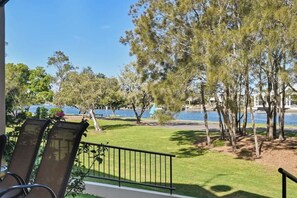 A balcony with chairs overlooking a grassy area and a body of water. - Beachport 16 Waterfront Views Apt (Mooloolaba)