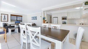 A modern living room with a dining area, white furniture, and a kitchen with white cabinets. - Lamer 1 Beach Access Courtyard Apt (Maroochydore)