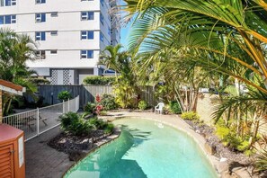 A swimming pool surrounded by tropical plants and a white fence, with a multi-story building in the background. - Lamer 1 Beach Access Courtyard Apt (Maroochydore)