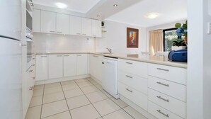 A modern kitchen with white cabinetry, a dishwasher, and a window with curtains. - Lamer 1 Beach Access Courtyard Apt (Maroochydore)