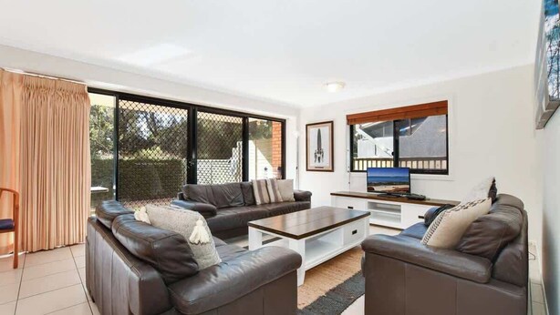 A modern living room with a sectional sofa, a coffee table, and a TV. - Lamer 1 Beach Access Courtyard Apt (Maroochydore)