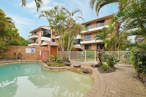 A modern building with a pool, surrounded by palm trees and a brick pathway. - Lamer 5 Beachfront Apt Mooloolaba (Maroochydore)