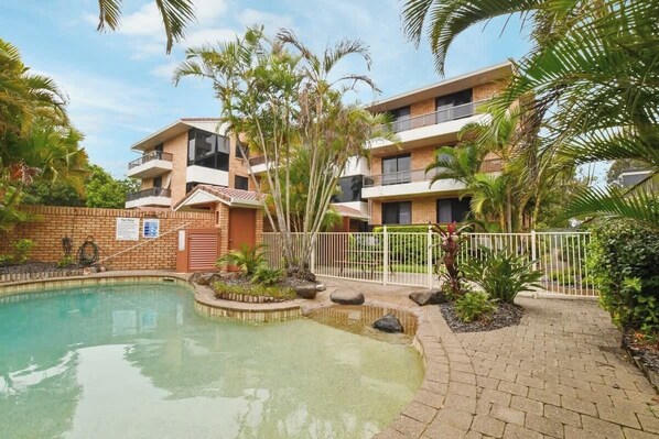A modern building with a pool, surrounded by palm trees and a brick pathway. - Lamer 5 Beachfront Apt Mooloolaba (Maroochydore)
