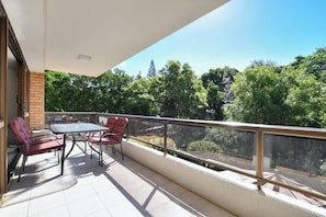 A balcony with a table and chairs, a glass railing, and a view of trees. - Lamer 5 Beachfront Apt Mooloolaba (Maroochydore)