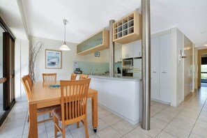 A modern kitchen with white cabinets, a central island, and a dining area with wooden chairs. - Lamer 5 Beachfront Apt Mooloolaba (Maroochydore)