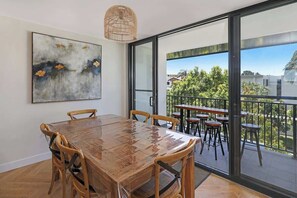 Ein Essbereich mit Holztisch und -stühlen, einem großen Gemälde an der Wand und einem Balkon mit Sitzgelegenheit im Freien.
