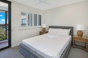A hotel room with a bed, two bedside tables, a window with shutters, and a view of the outdoors.