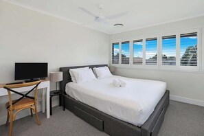 Ein Hotelzimmer mit einem Bett, einem Schreibtisch mit Computer, einem Stuhl, einem Deckenventilator und einem Fenster mit Jalousien.