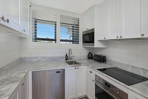 A modern kitchen with white cabinets, a stainless steel dishwasher, a black induction cooktop, and a microwave.