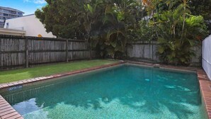 Piscina retangular com indicador de profundidade de 1,0m, cercada por uma vedação de madeira e vegetação exuberante.