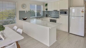 Cozinha moderna com armários brancos, uma ilha central, micro-ondas e geladeira.