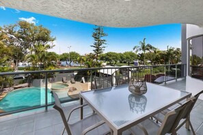 Ein Balkon mit Glastisch und Stühlen, mit Blick auf einen Swimmingpool und üppiges Grün.