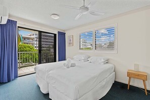 Une chambre d’hôtel avec un lit, un ventilateur de plafond, une fenêtre avec des stores, une table de chevet et une vue sur l’extérieur.