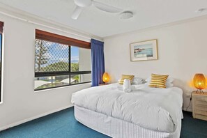 Un dormitorio con cama, ventana con vistas, ventilador de techo y mesita de noche con lámpara.