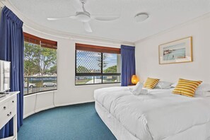 Ein Hotelzimmer mit Bett, Schreibtisch, Stuhl, Deckenventilator, Fenster mit Blick und einem gerahmten Bild an der Wand.