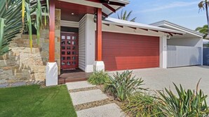 A modern house with a red garage, stone facade, and a well-maintained lawn. - Adelong Waterfront Home Mooloolaba (Buddina)
