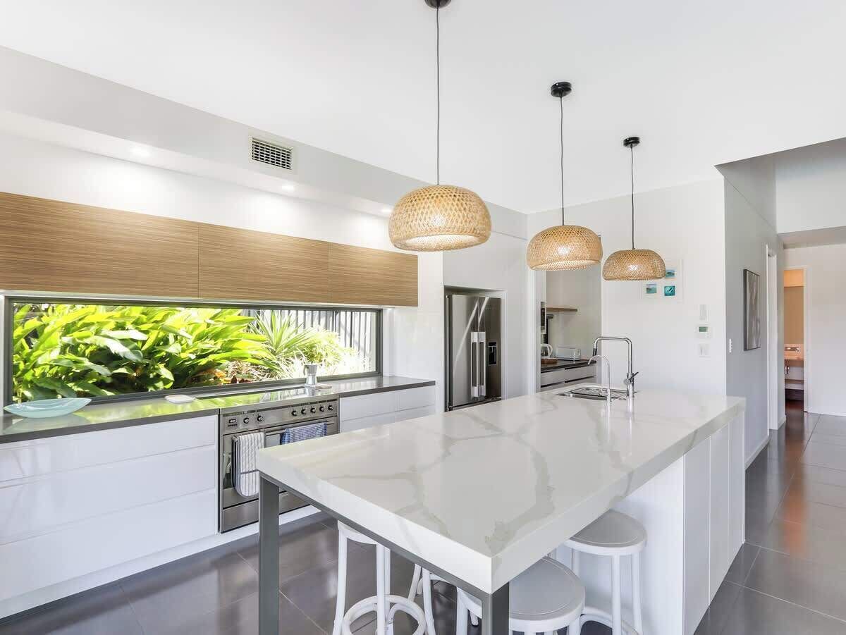 Una cocina moderna con una isla grande, electrodomésticos de acero inoxidable y vistas al verdor exterior.