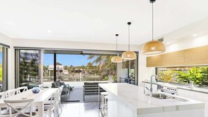 A modern kitchen with a large island, white cabinetry, and pendant lighting. - Adelong Waterfront Home Mooloolaba (Buddina)