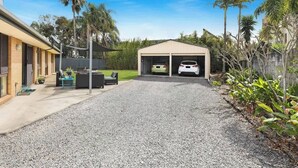 A residential driveway with a covered garage, a patio with outdoor furniture, and a lawn. - Naroo 7 Central Mooloolaba Stay (Mooloolaba)