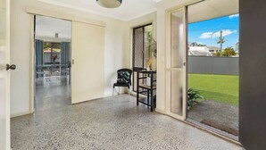 A spacious room with a large sliding glass door leading to a balcony, a ceiling light fixture, and a chair with a table. - Naroo 7 Central Mooloolaba Stay (Mooloolaba)